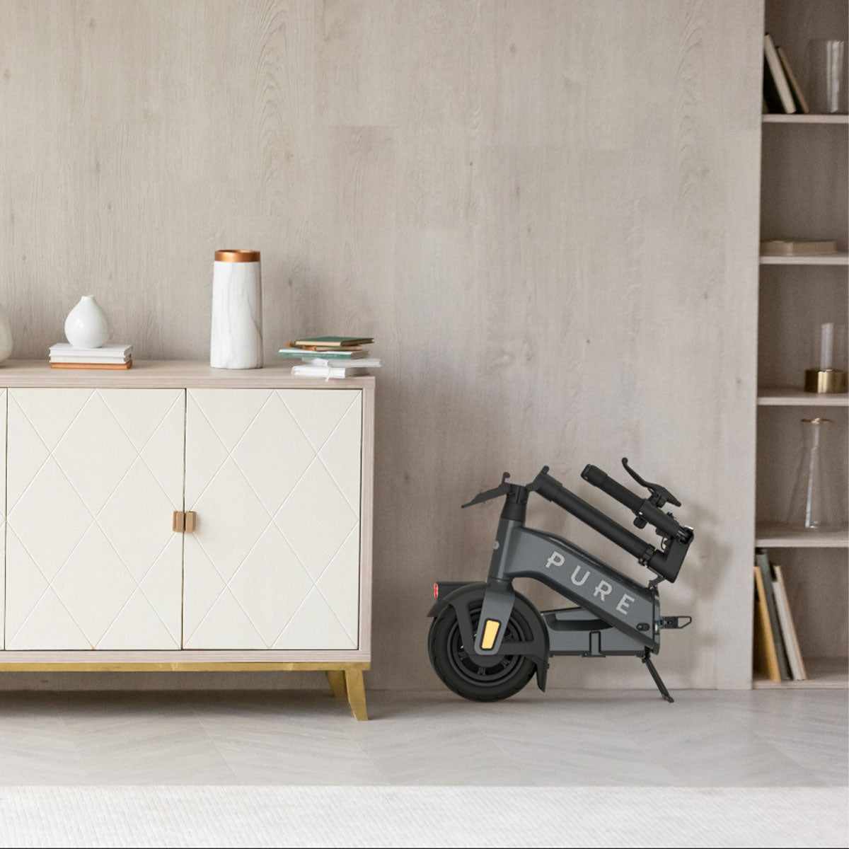Pure Advance Flex Electric Scooter folded next to cabinet - Mercury Grey