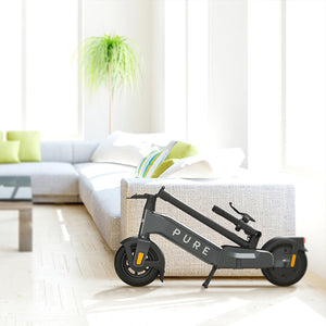 Pure Advance+ Electric Scooter folded next to sofa - Mercury Grey